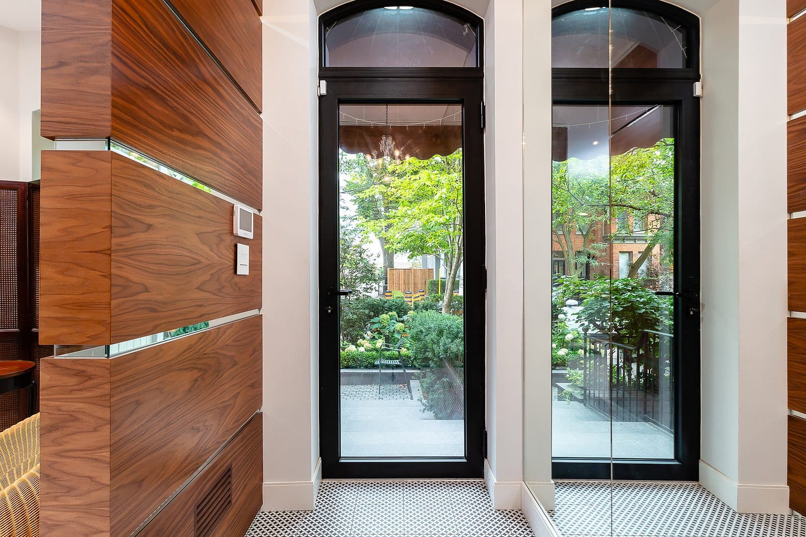Walnut paneled vestibule with penny tile flooring and black framed glass doors opening to a rear garden.