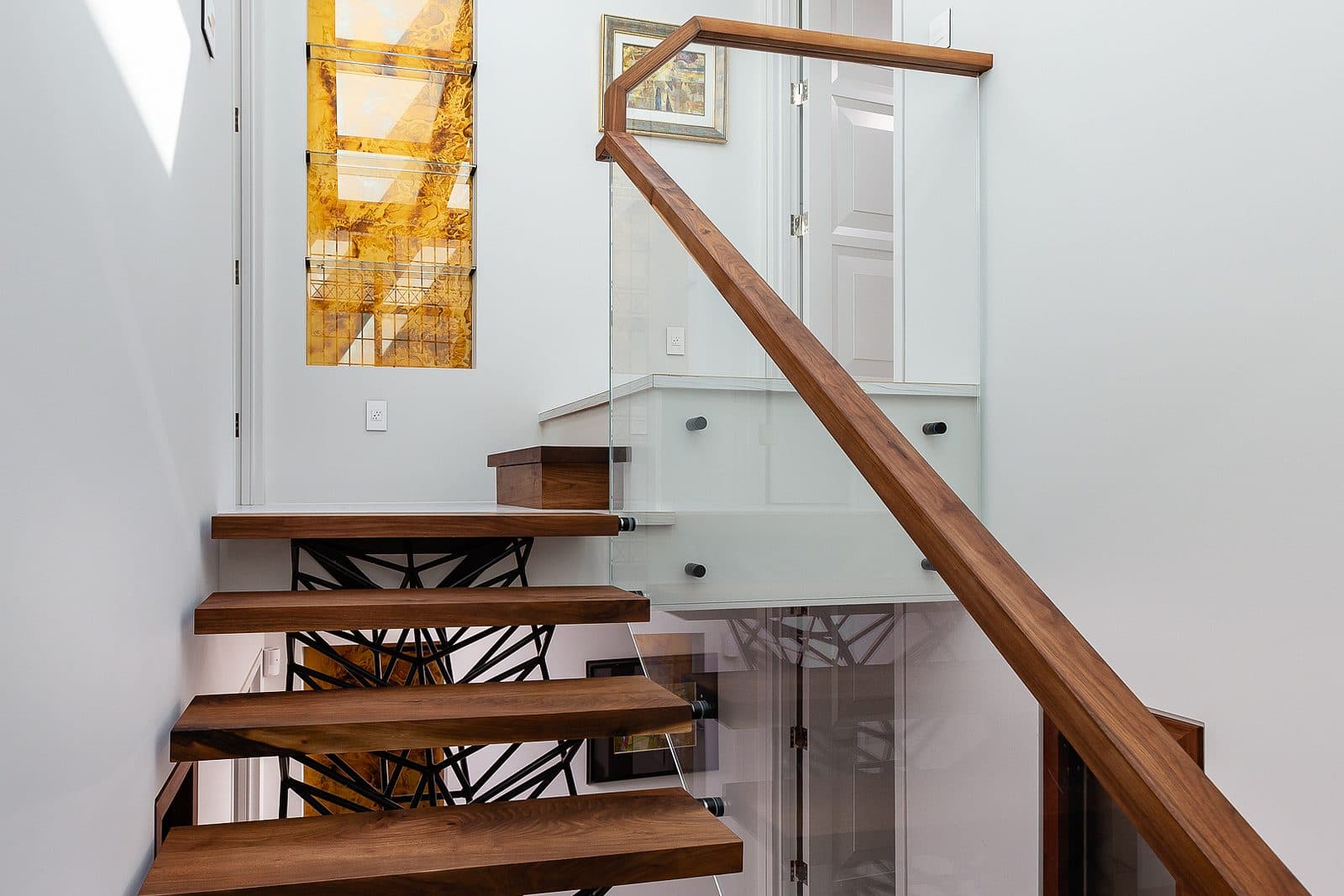 Close view of a black steel lattice grid panel beside a walnut framed skylight window at the stair landing.