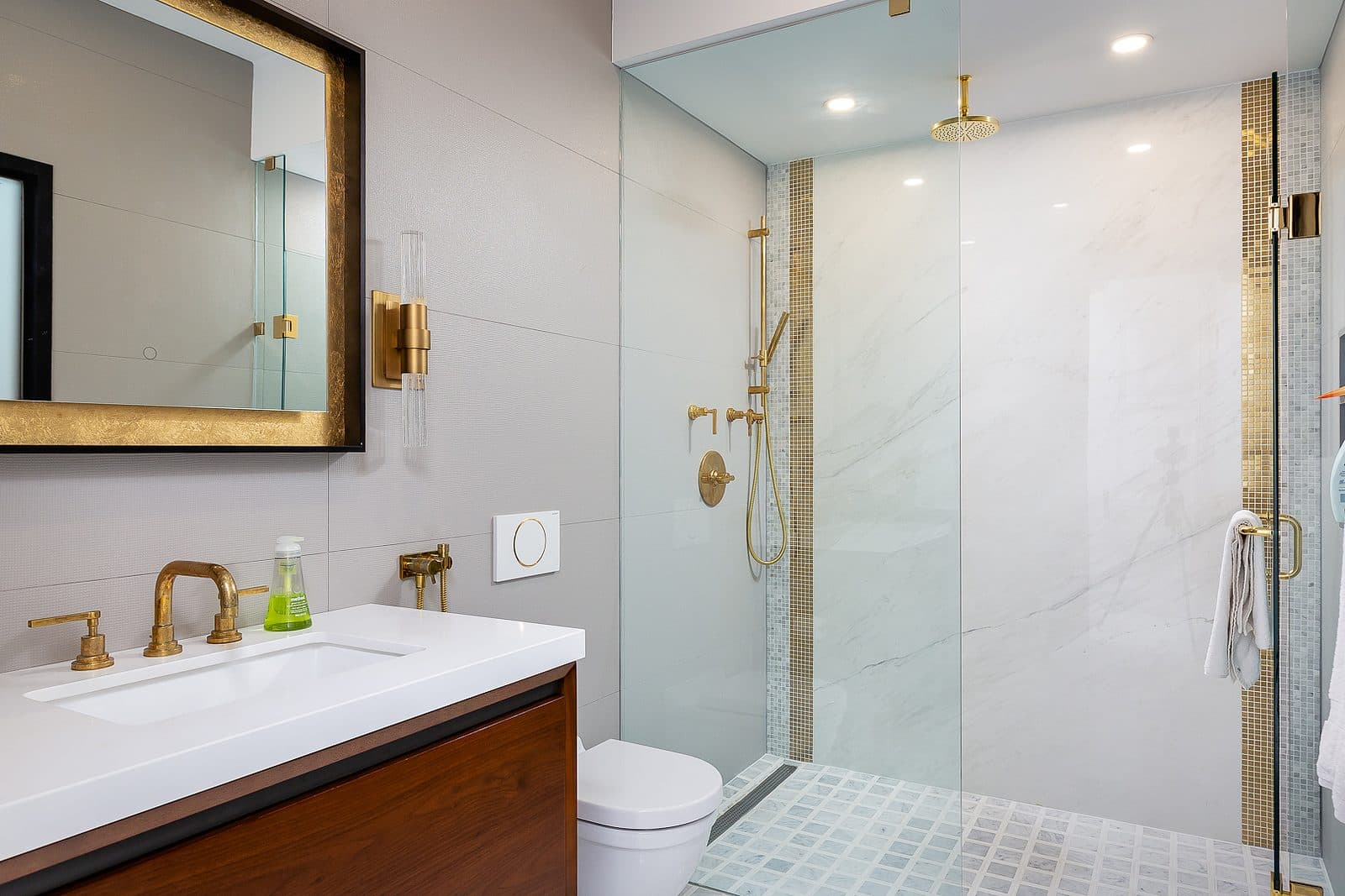 Walk-in glass shower with book matched marble wall, black rain shower head, and matte black fixtures beside a walnut vanity.