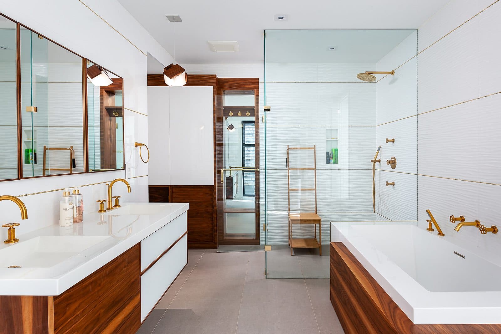 Symmetrical bathroom with walnut double vanity, brass fixtures, mirrored medicine cabinets, and a soaking tub in walnut surround.