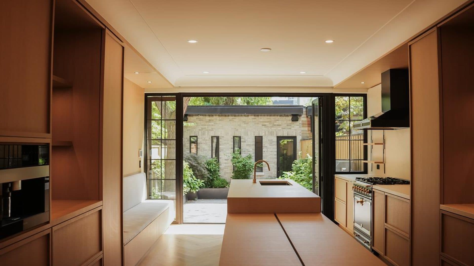 Oak kitchen and banquette opening through glazed doors to a stone courtyard