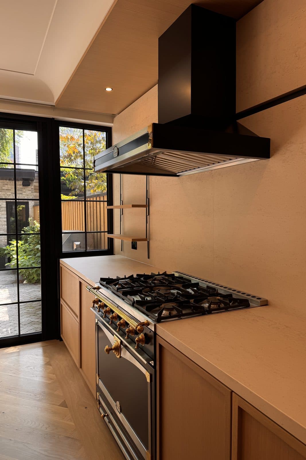 Kitchen with black range hood and oak cabinetry beneath tall steel windows