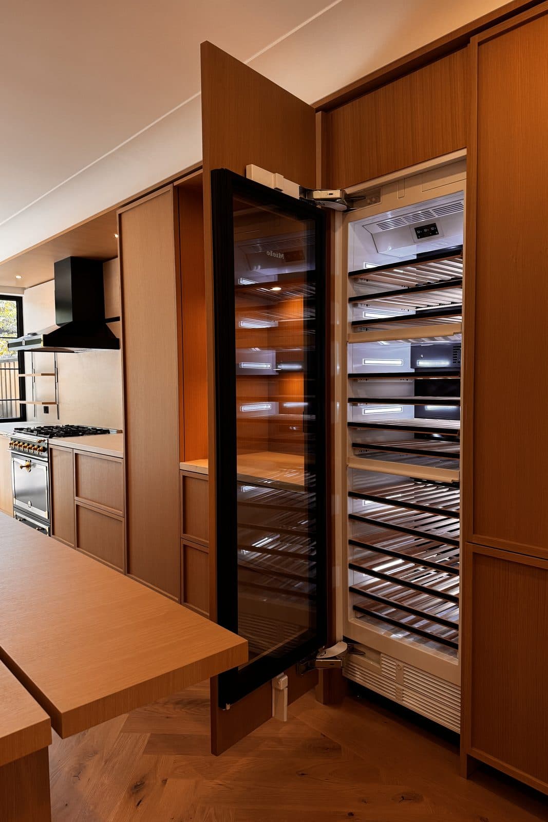 Glass-front wine column built into oak millwork beside a dining table