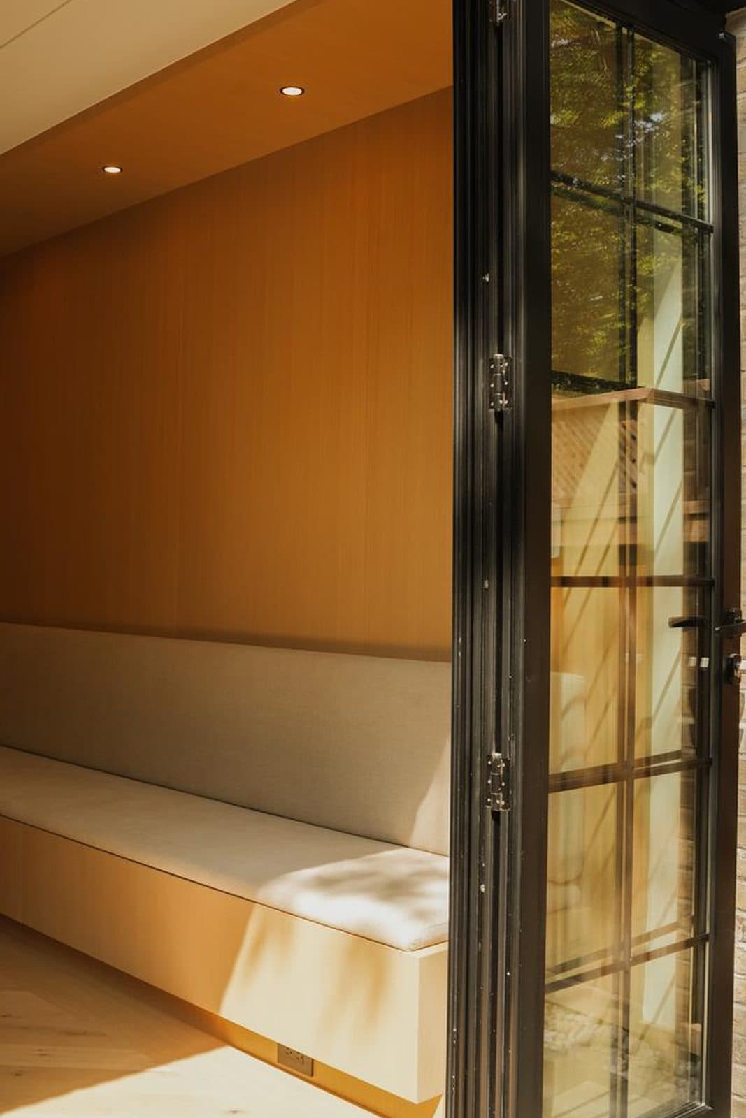 Cushioned window bench beside black steel-framed glazed doors