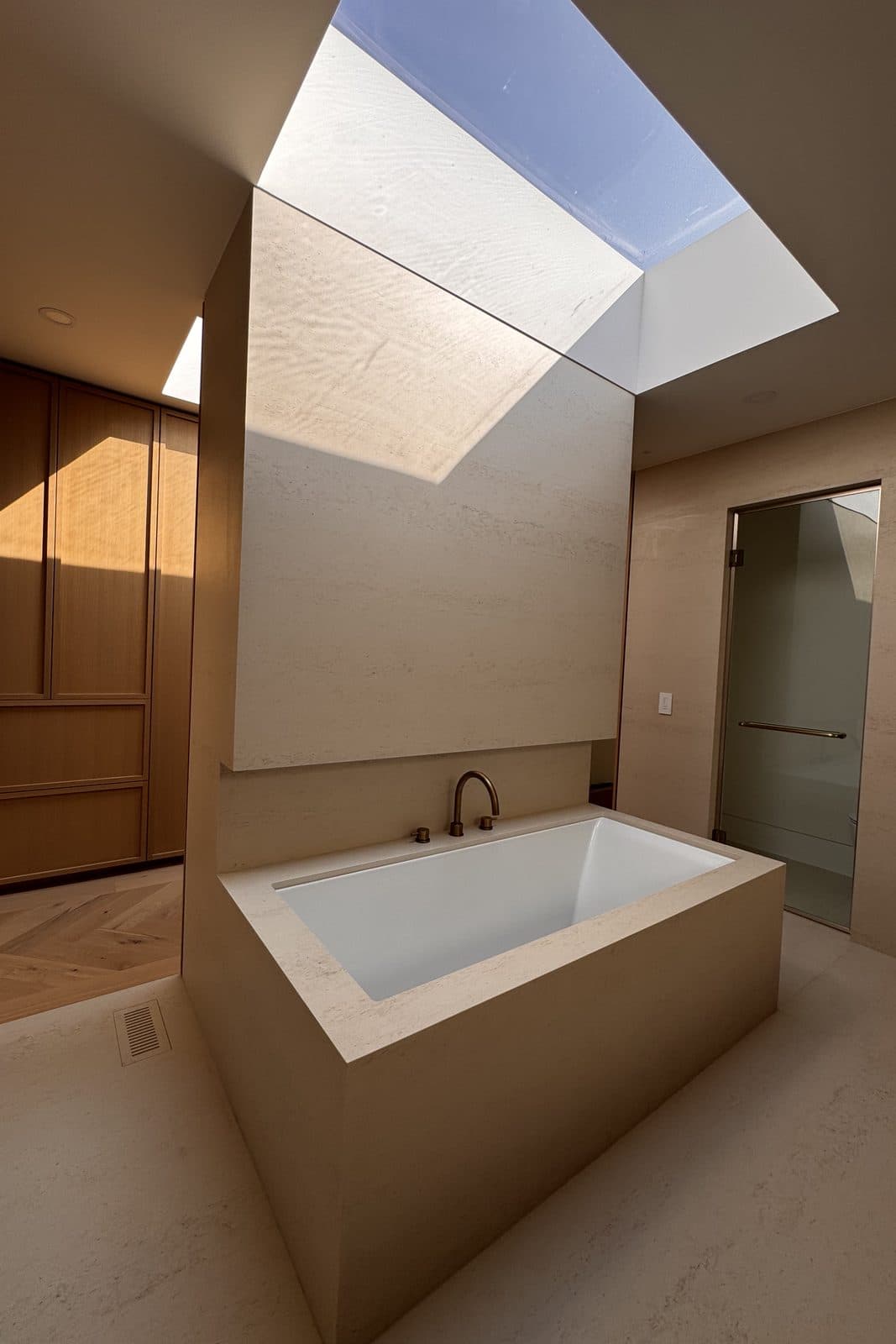 Freestanding soaking tub beneath a skylight in an oak-lined bathroom