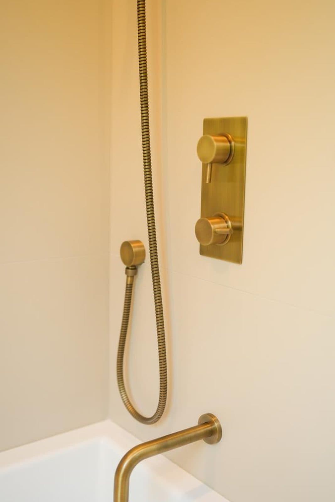 Detail of brass shower fittings mounted above a bathtub
