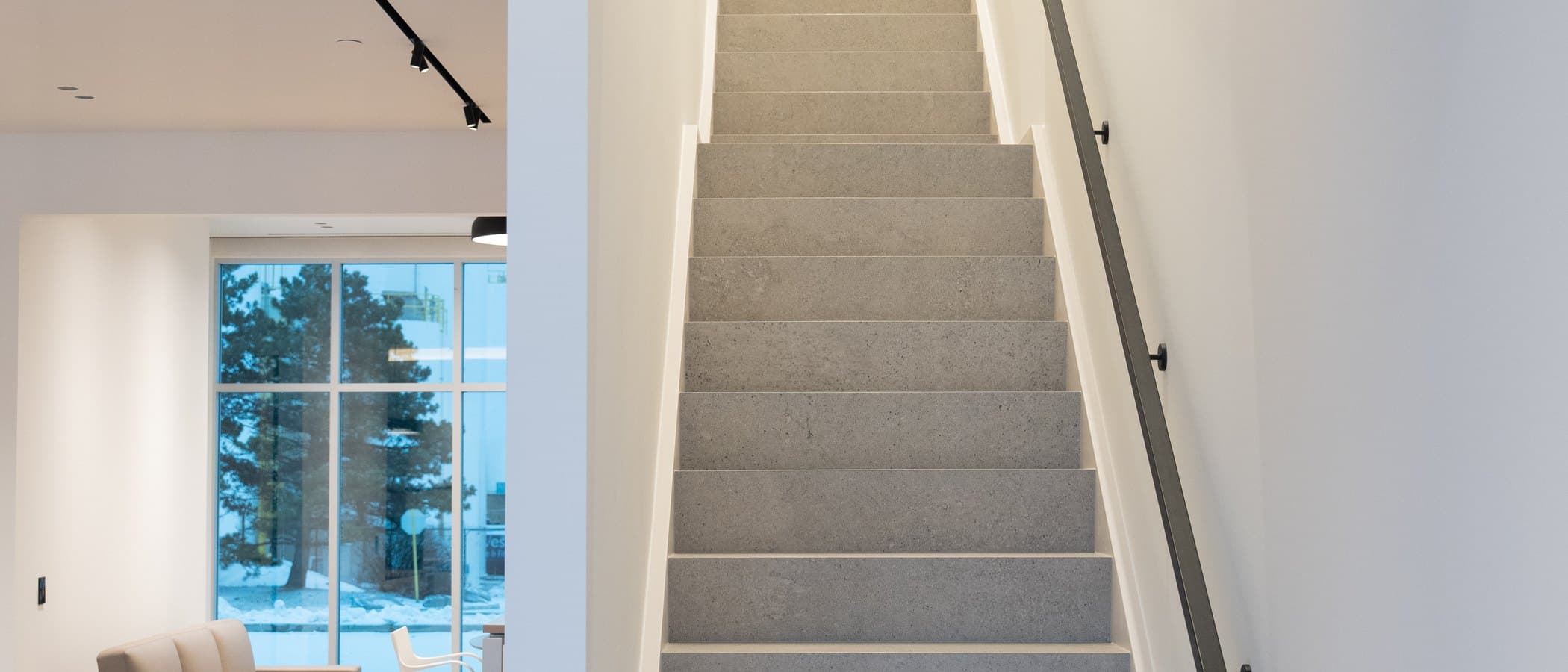 Terrazzo staircase rising past a lounge chair toward bright upper floors