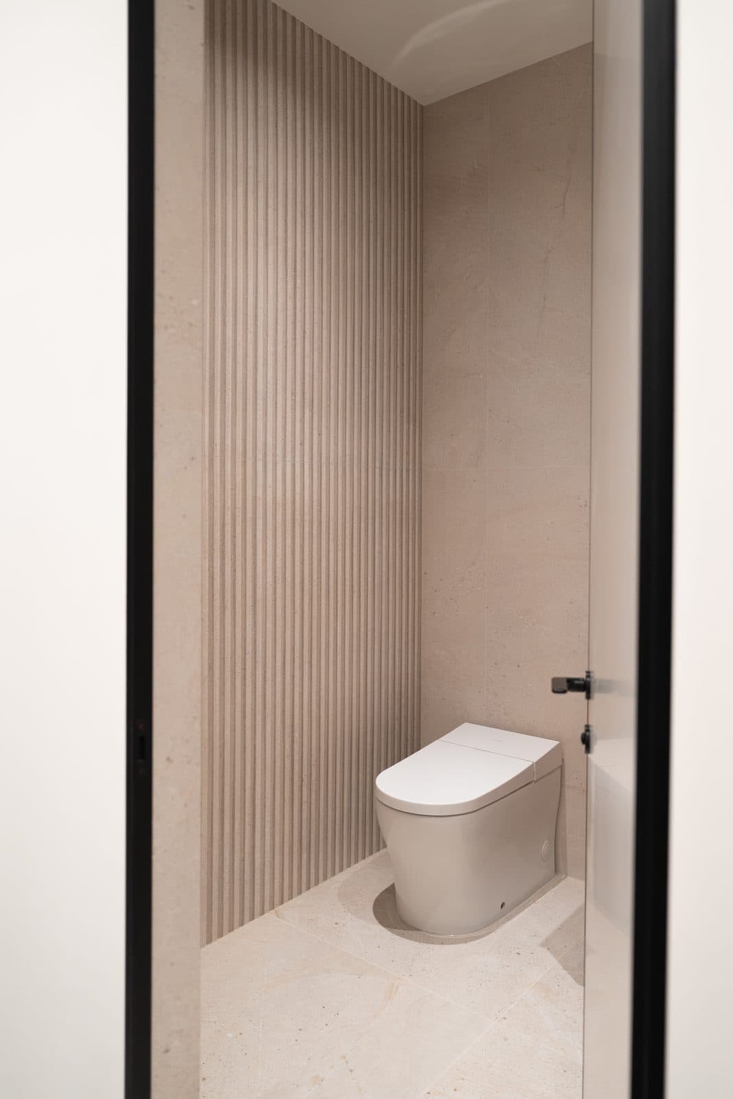 Washroom with a fluted stone wall seen through a black framed door