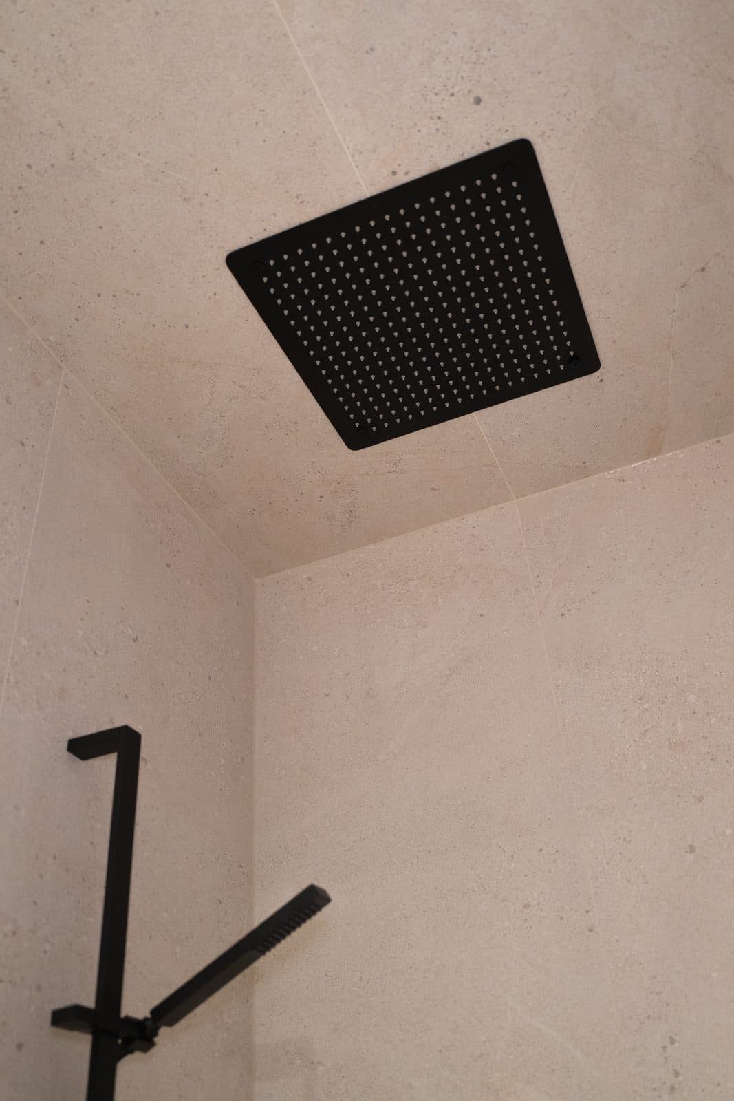 Black rain shower head set into the ceiling above stone tile