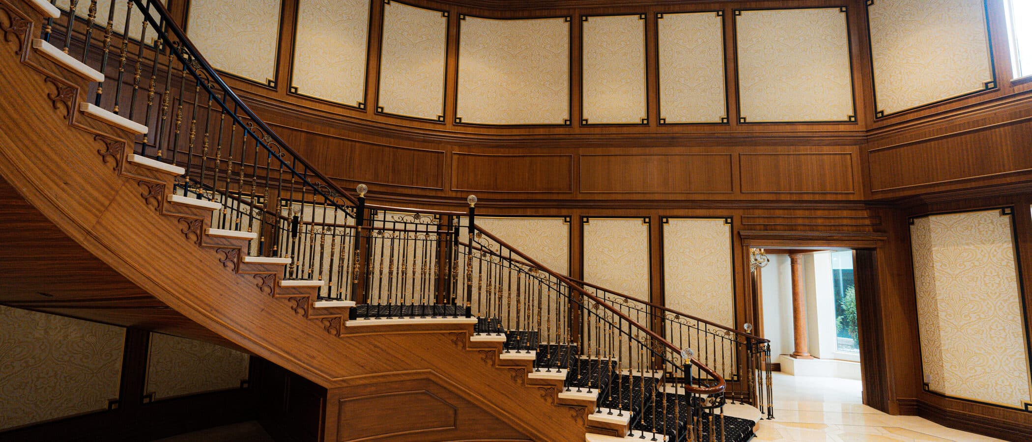 Curved staircase and wrought iron balustrade beneath panelled walls