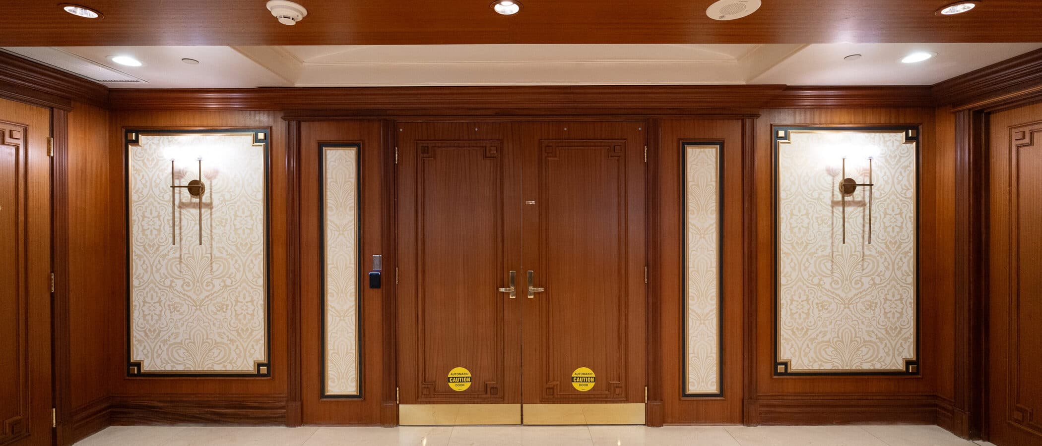 Mahogany elevator lobby with panelled doors and wall sconces
