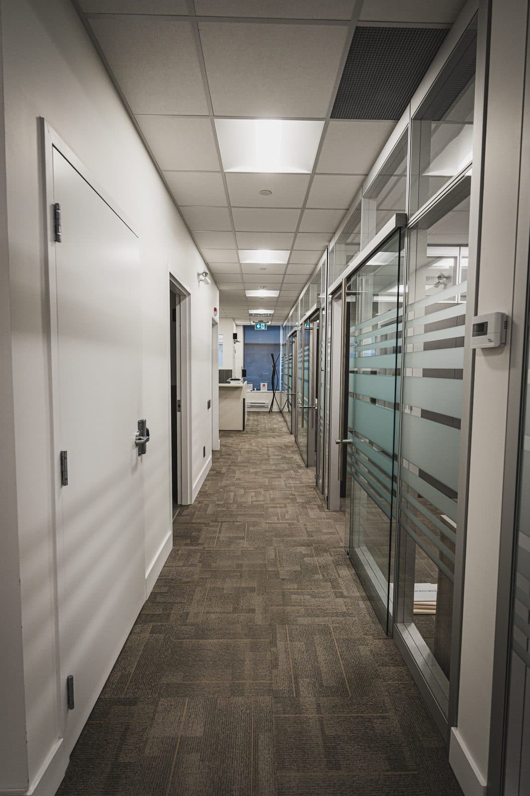 Long glazed corridor lined in striped privacy film, with a card reader mounted on the aluminum mullion.