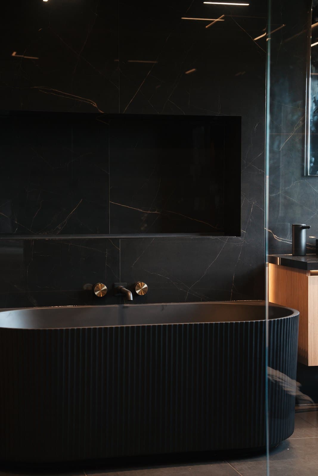 Fluted black marble freestanding tub against book matched stone with brass fittings