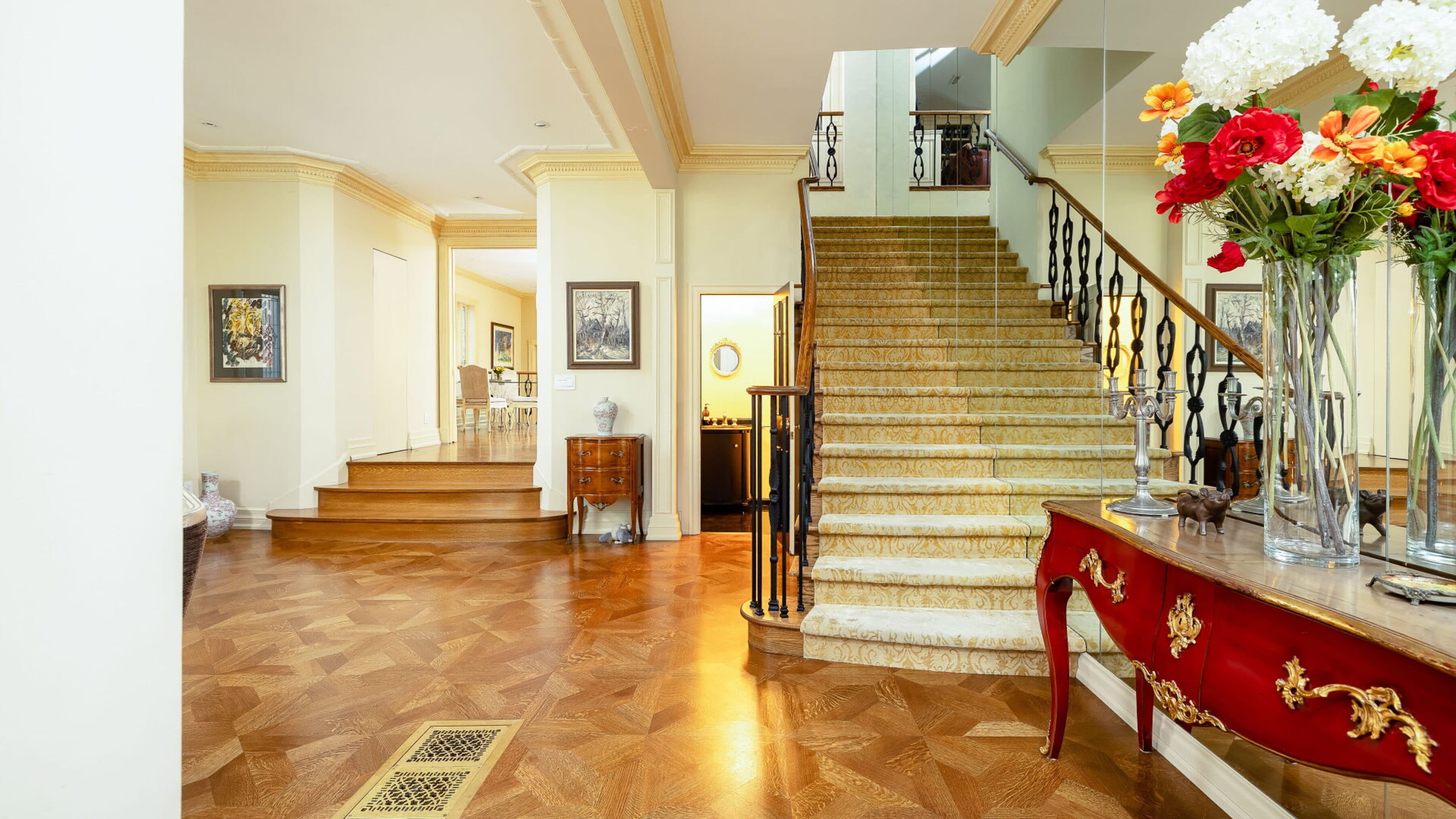 Curved staircase with an iron balustrade and a red console on herringbone floors
