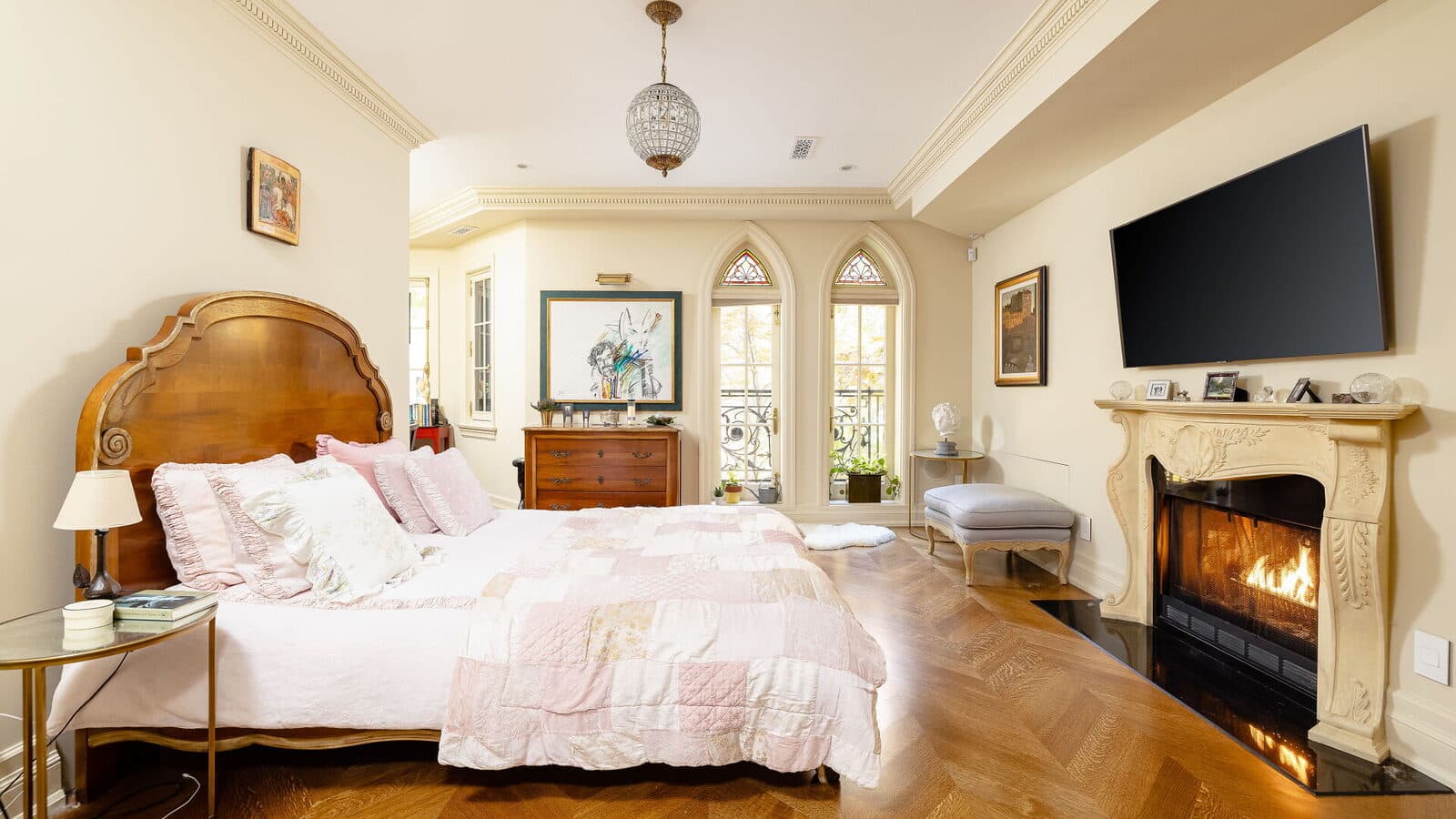 Primary bedroom with a lit fireplace and gothic arched windows