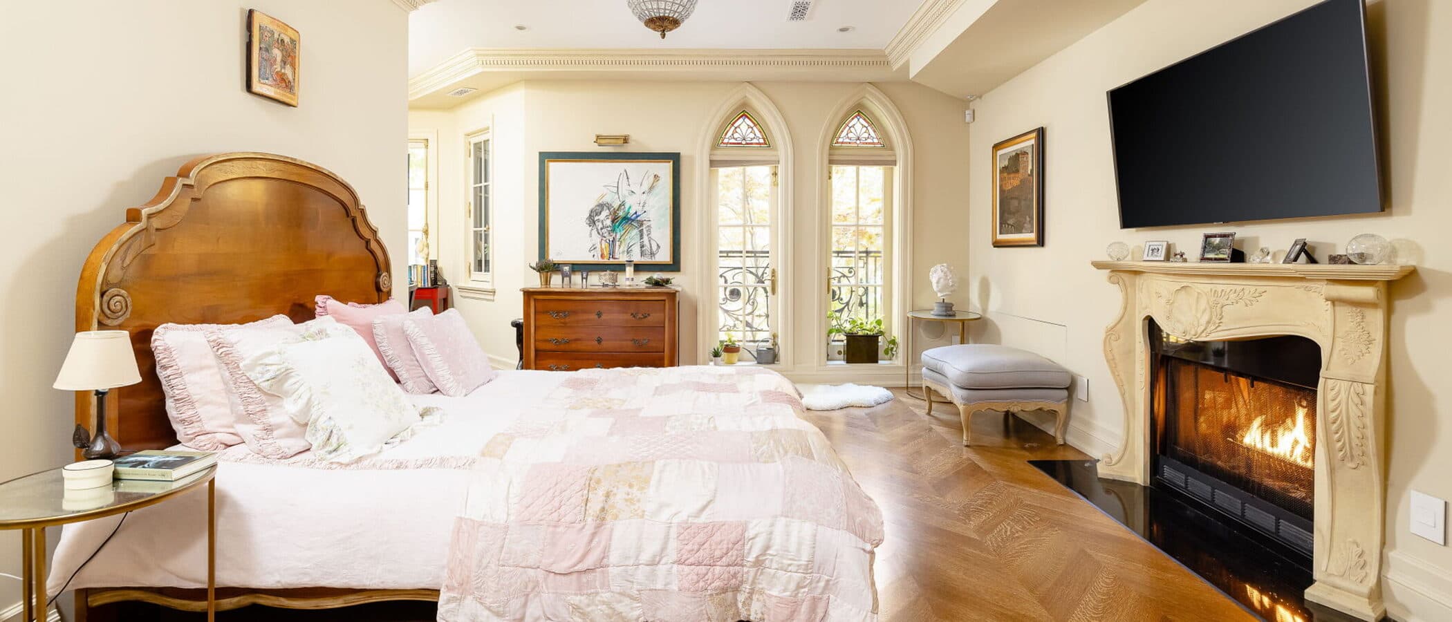 Primary bedroom with a lit fireplace and gothic arched windows