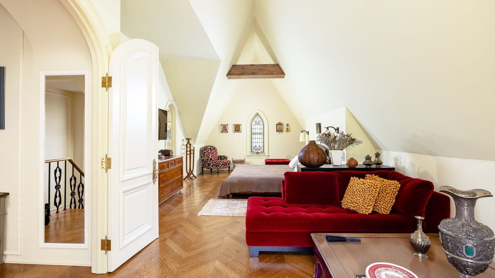 Attic sitting room with a red velvet sectional beneath exposed beams and stained glass