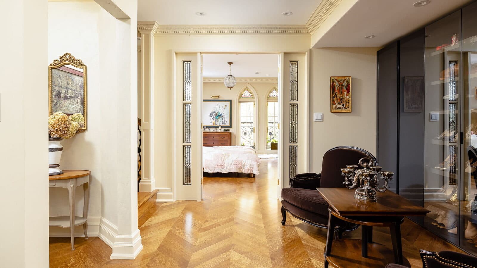 Chevron floor hallway leading into the primary suite past stained glass sidelights
