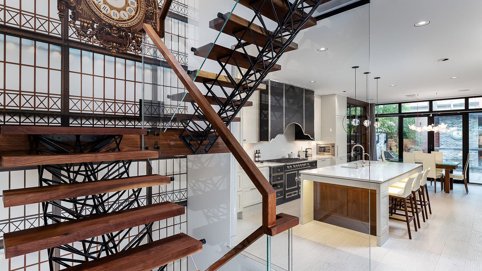 Spiral stair beside a glazed wall with a large station clock and the kitchen beyond