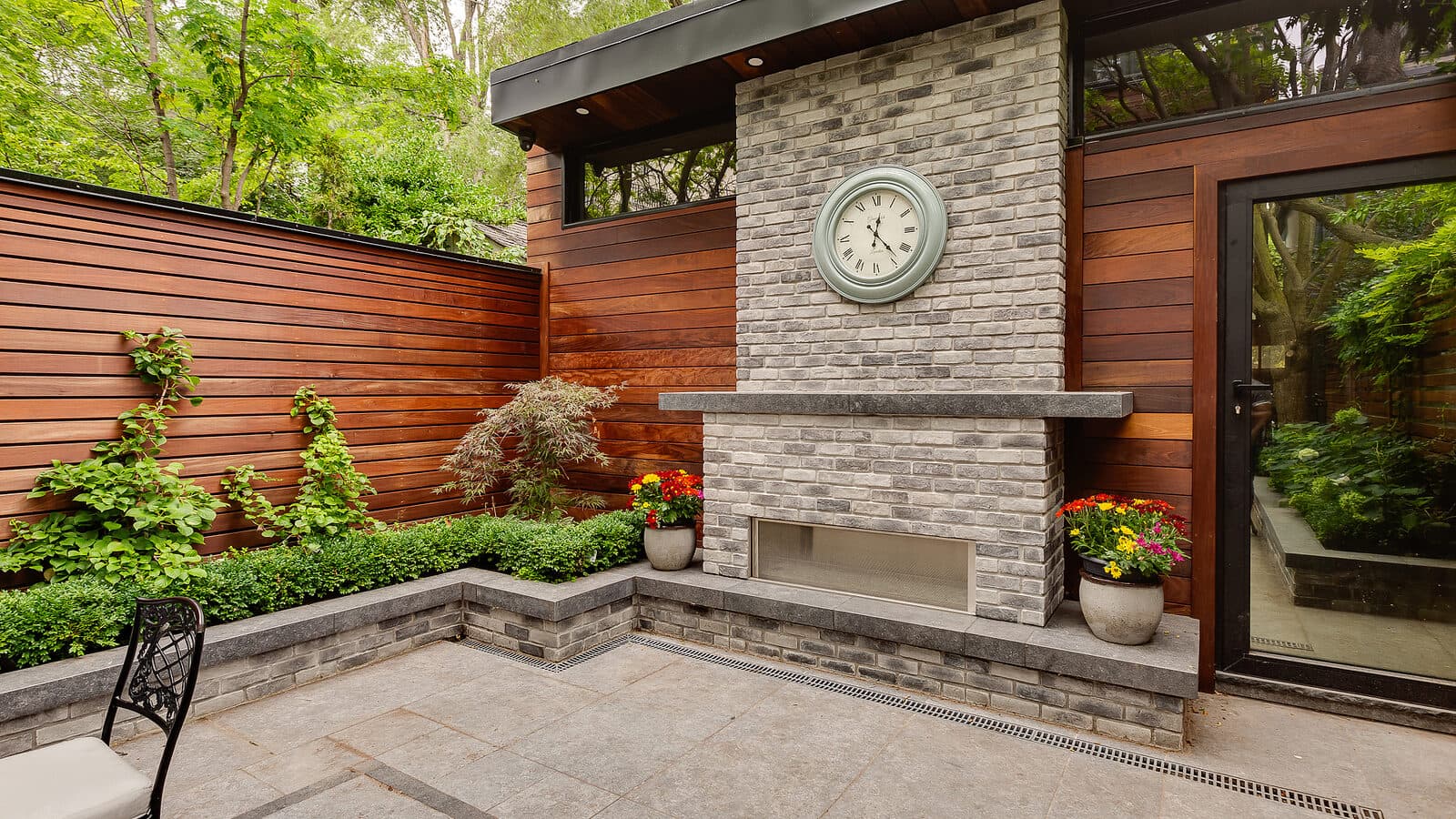 Courtyard fireplace corner with a wall clock, ipe fence and layered planting