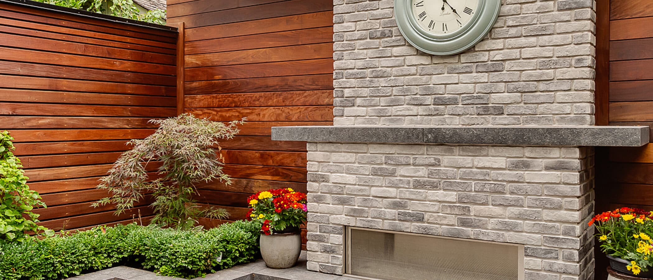 Courtyard fireplace corner with a wall clock, ipe fence and layered planting