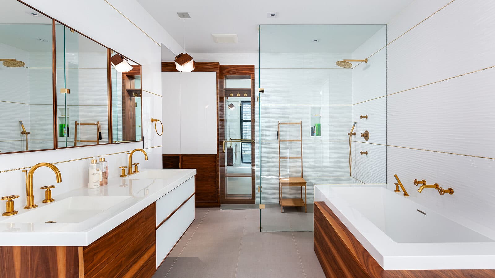 Symmetrical bathroom with walnut double vanity, brass fixtures, mirrored medicine cabinets, and a soaking tub in walnut surround