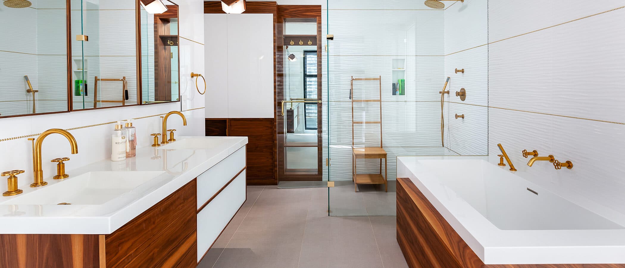 Symmetrical bathroom with walnut double vanity, brass fixtures, mirrored medicine cabinets, and a soaking tub in walnut surround