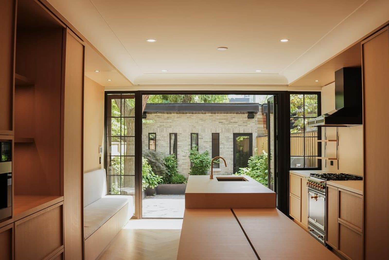 Oak kitchen and banquette opening through glazed doors to a stone courtyard