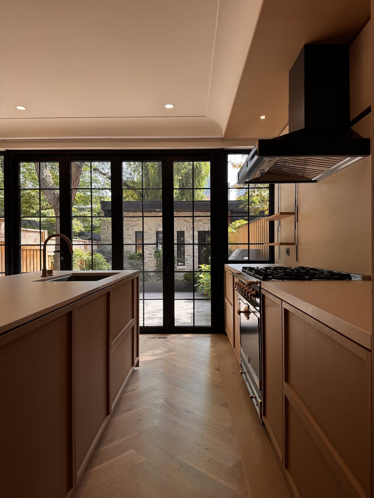 Kitchen with an island, brass faucet and range opening through a steel framed glass wall to the courtyard