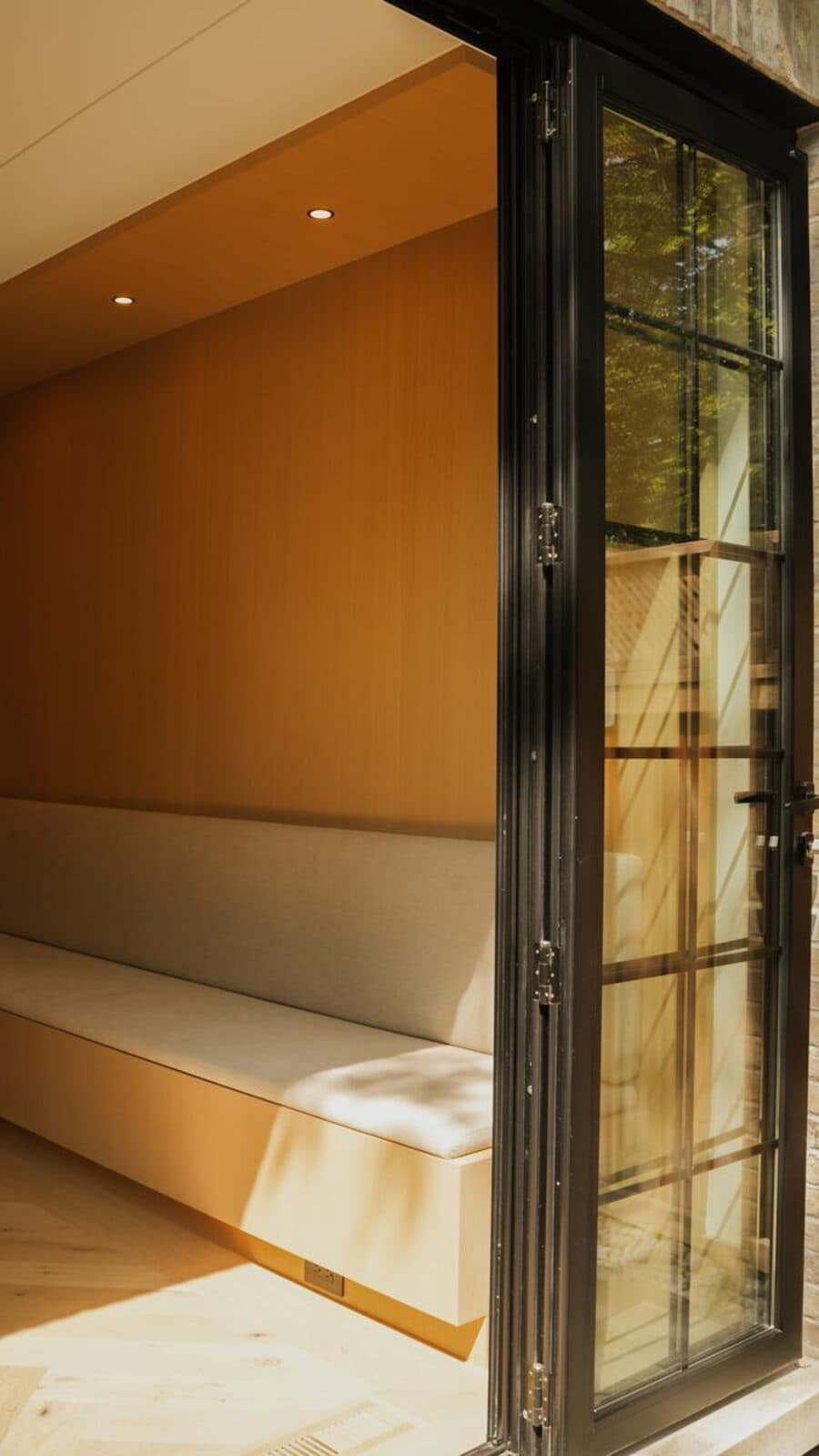 Cushioned window bench beside black steel framed glazed doors