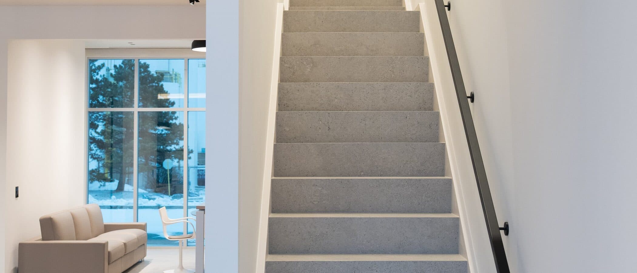 Terrazzo staircase rising past a lounge chair toward bright upper floors