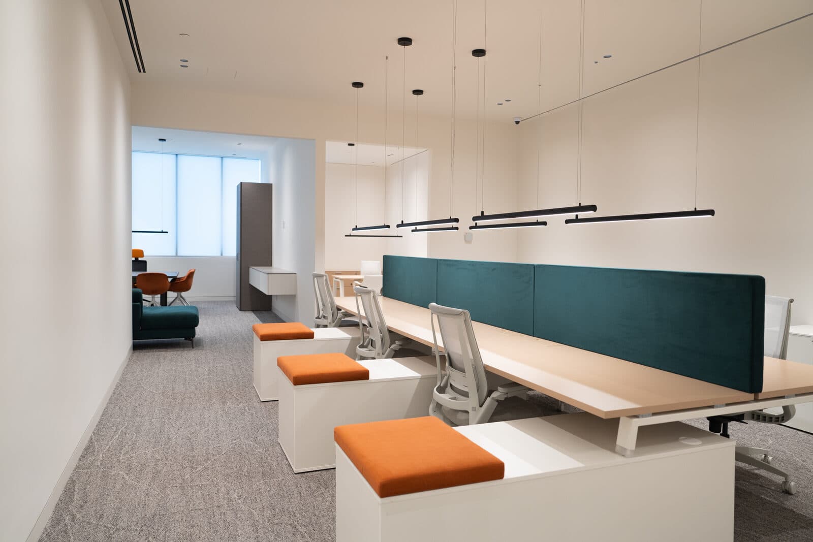 Workstations with orange stools beneath black linear pendants