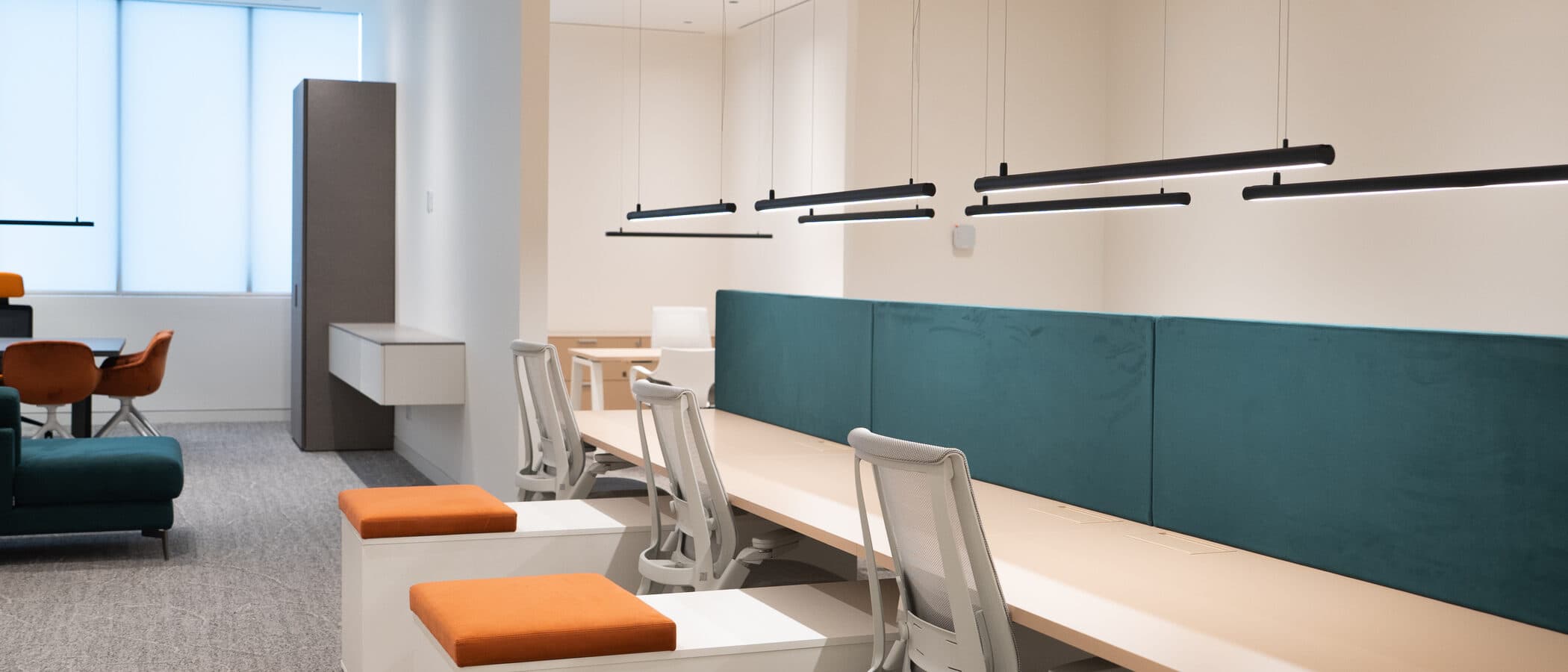 Workstations with orange stools beneath black linear pendants