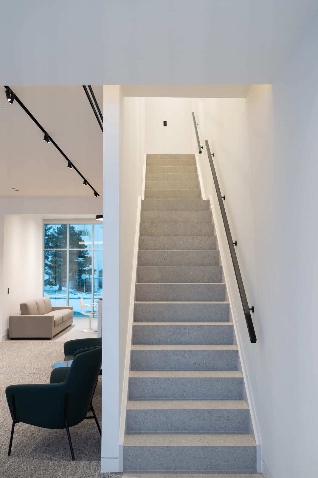 Terrazzo staircase rising past a lounge chair toward bright upper floors