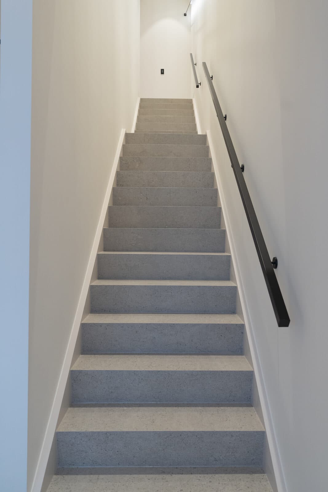 Terrazzo staircase with a black handrail between white walls