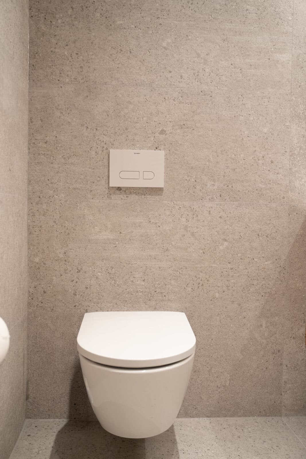 Wall hung toilet and flush plate against stone tile
