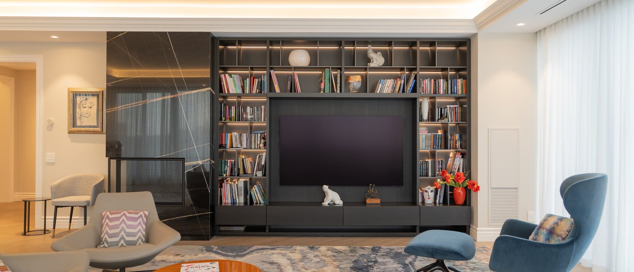 Library wall with built-in walnut shelving, art books and a pair of armchairs