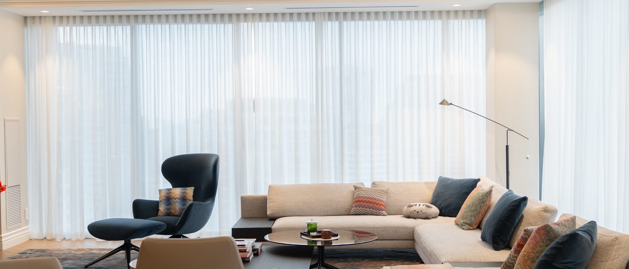 Living room with floor-to-ceiling drapery, sectional seating and a wing chair arranged around a coffee table