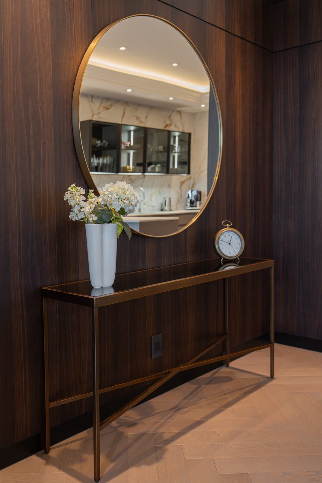 Walnut foyer wall with a console, clock and a mirror reflecting the kitchen