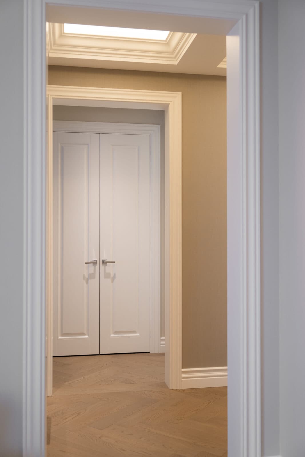 Hallway through a cased opening toward double doors beneath a skylight cove