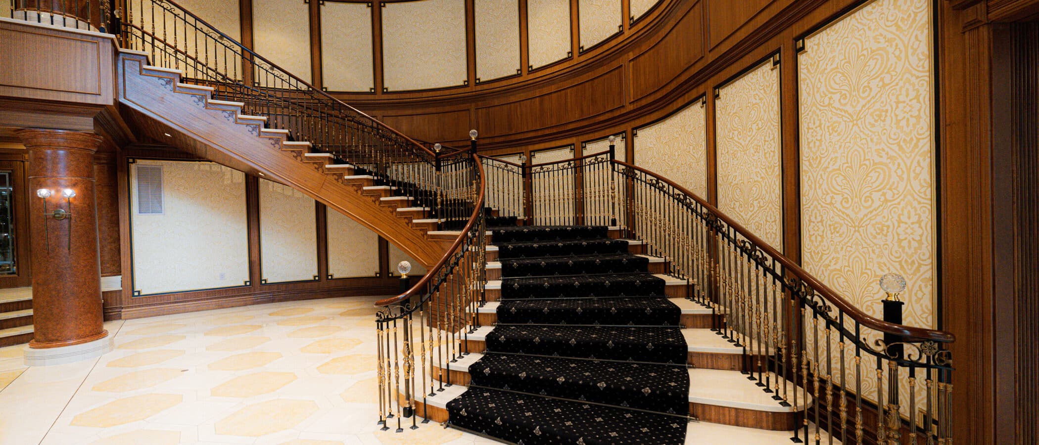 Sweeping mahogany staircase with a patterned black runner in the Avignon lobby