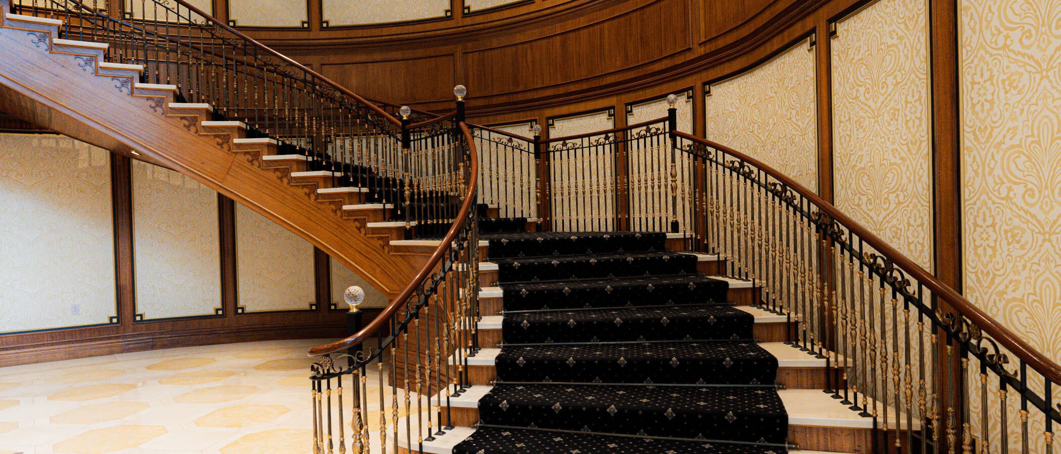 Sweeping mahogany staircase with an iron balustrade and gilded wall panels