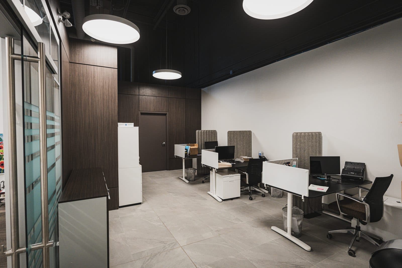Open workstations beneath a black ceiling, walnut millwork wall, and large format stone tile flooring in a corporate office fit out.