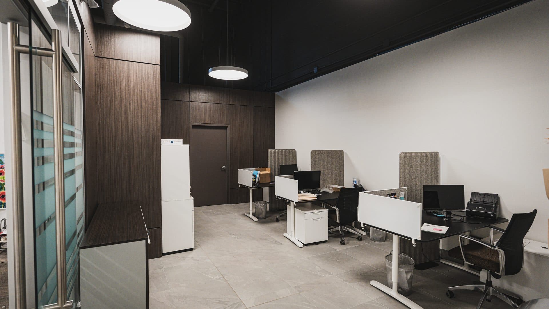 Open workstations beneath a black ceiling, walnut millwork wall, and large format stone tile flooring in a corporate office fit out.
