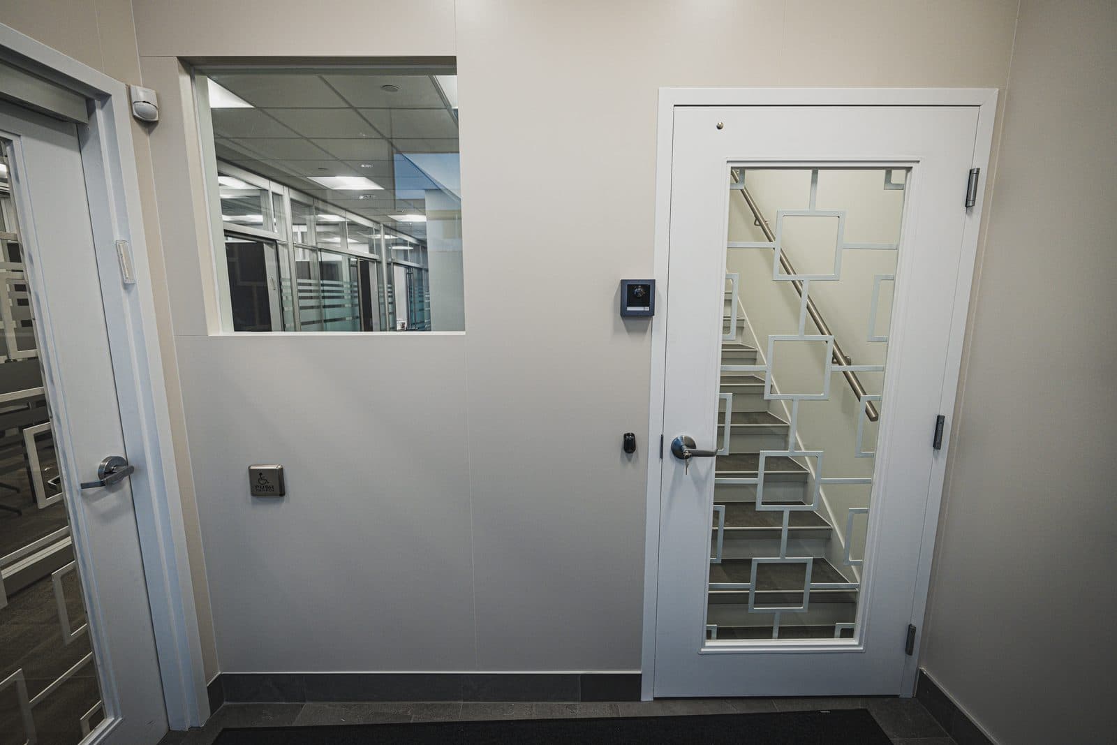 Corridor junction with an interior window onto open plan workstations and a door glazed in a geometric grille pattern.