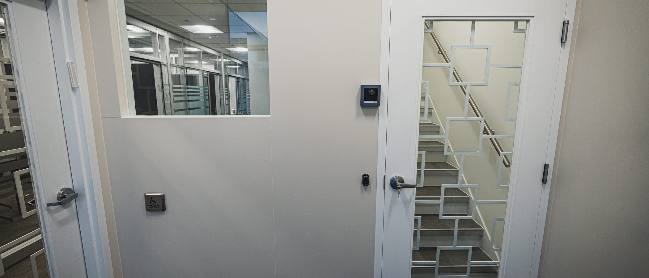 Corridor junction with an interior window onto open plan workstations and a door glazed in a geometric grille pattern.