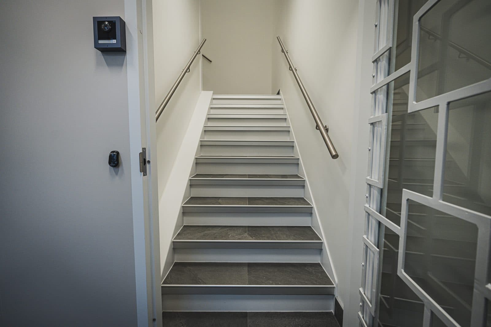 Stairwell landing finished in stone treads, viewed beside a glazed interior window and an access controlled door.