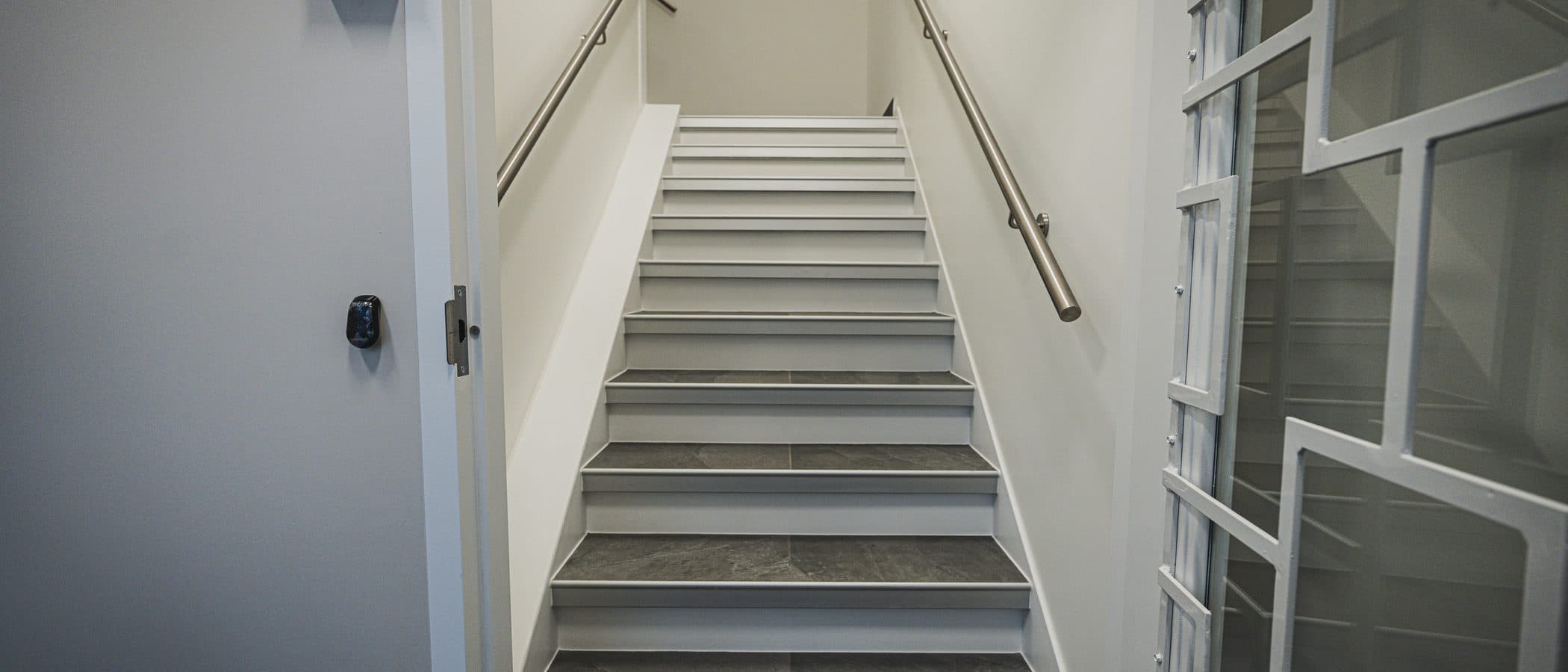Stairwell landing finished in stone treads, viewed beside a glazed interior window and an access controlled door.