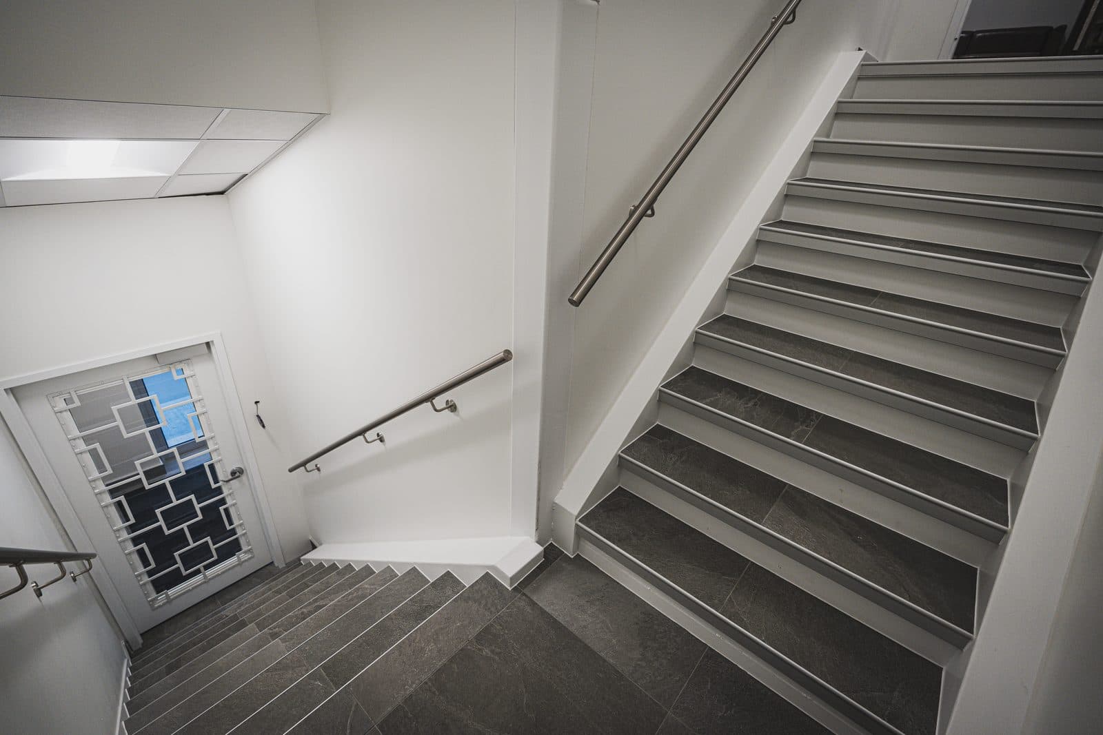 Dramatic downward view of a stone tread staircase with a stainless steel handrail descending along a diagonal line.