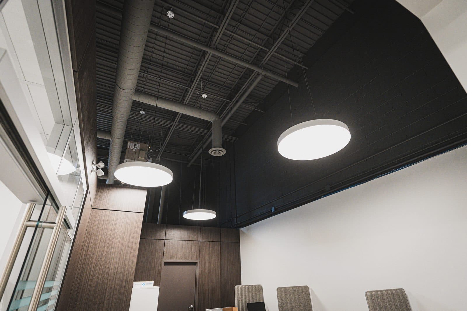 Pendant drum lights and exposed ductwork above a walnut millwork corner with two doors set into the paneling.